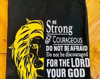May include: Black t-shirt featuring a yellow lion graphic and white text that reads "Be Strong & Courageous Do Not Be Afraid Do Not Be Discouraged For The Lord Your God Will Be With You Wherever You Go Joshua 1:9"