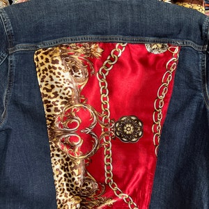 May include: A denim jacket with a red, gold, and brown patterned fabric panel on the back. The fabric panel features a chain design and a leopard print.