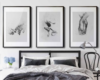 May include: Three black framed prints of black and white pencil drawings of hands. The prints are hanging on a white wall above a bed with white bedding and gray throw blankets.