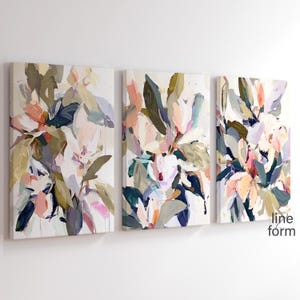 May include: A set of three abstract floral paintings in shades of pink, green, blue, and white. The paintings are on canvas and have a textured finish. The paintings are arranged in a row on a white wall.