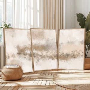 May include: Three abstract paintings in beige and brown tones with a white background. The paintings are framed in a light wood frame and are hanging on a white wall.