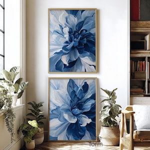 Op de afbeelding: Twee ingelijste bloemenkunstprints. Elke print toont een grote, abstracte bloem in tinten blauw en wit. Het kunstwerk wordt tentoongesteld in een kamer met planten en een houten boekenkast.