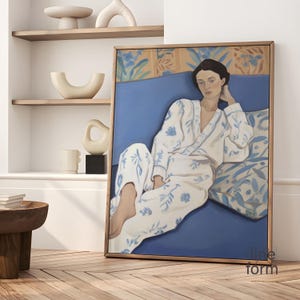 Peut inclure: Une peinture encadrée d'une femme en robe blanche et bleue à motifs floraux, allongée sur un canapé bleu avec un coussin à motifs. L'arrière-plan est un motif floral jaune et vert.
