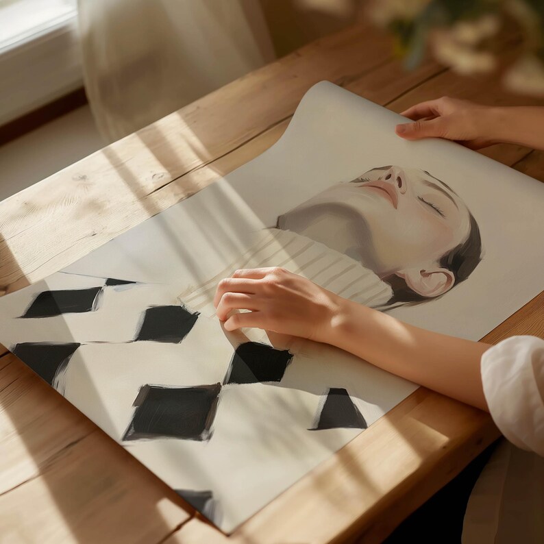 Puede incluir: Una impresi&oacute;n que presenta un retrato de una mujer con los ojos cerrados, que lleva un su&eacute;ter. La impresi&oacute;n tiene un patr&oacute;n geom&eacute;trico en blanco y negro en la parte inferior. La obra de arte se exhibe sobre una superficie de madera.