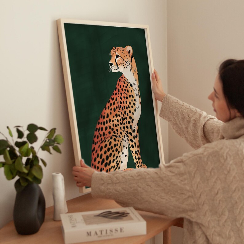 May include: A framed print of a cheetah sitting on a dark green background. The cheetah is facing to the left and has a spotted coat with orange and black markings.