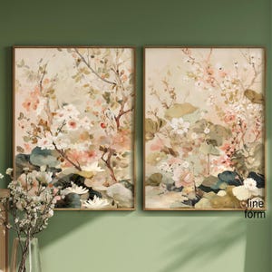 May include: Two framed floral art prints. The artwork features a soft, watercolor style with a palette of pink, white, and green. The botanical theme includes flowers, leaves, and branches, set against a neutral background. The frames are a warm brown.