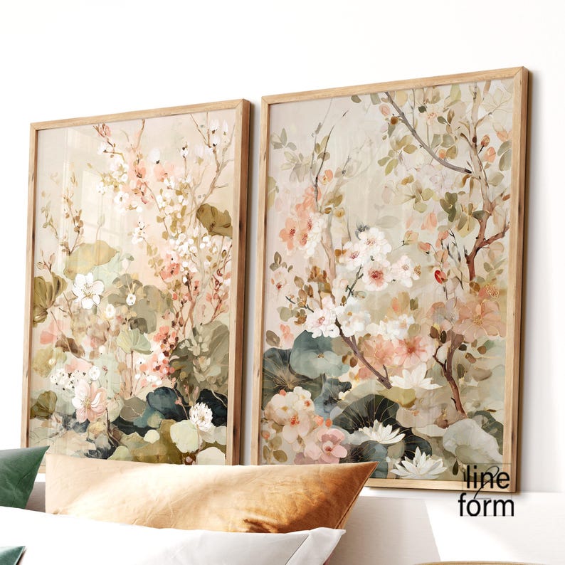 May include: Two framed floral art prints. The artwork features a watercolor style with soft pink, white, and green flowers and foliage. The frames are light-colored wood, and the overall aesthetic is delicate and natural.