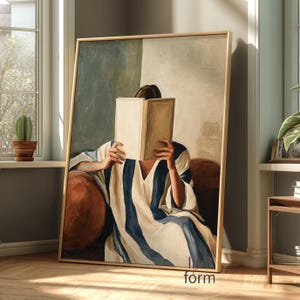 Puede incluir: Una impresión artística enmarcada representa a una persona leyendo un libro, con el libro cubriendo su rostro. La persona lleva una prenda a rayas blancas y azules. La obra de arte está en una habitación con luz natural.