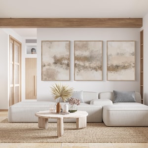 May include: A white sectional sofa with three cushions, a coffee table, and three abstract paintings on the wall. The sofa is in a living room with a wooden beam ceiling and a large window.