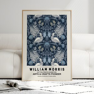 Pu&ograve; includere: Una stampa incorniciata con un design simmetrico con uccelli ed elementi floreali nei toni del blu, grigio e crema. La stampa include il testo "WILLIAM MORRIS" e "COTTON PRINTS EXHIBITION ARTS & CRAFTS PIONEER".