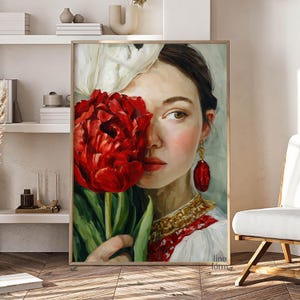 Puede incluir: Retrato enmarcado de una mujer sosteniendo una gran flor roja, que le cubre parcialmente la cara. Viste un vestido blanco con bordados rojos y joyas doradas. La obra tiene un estilo suave y pict&oacute;rico.
