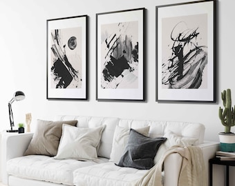 May include: Three black and white abstract art prints in black frames are displayed on a white wall above a white couch with beige, white, and gray throw pillows.