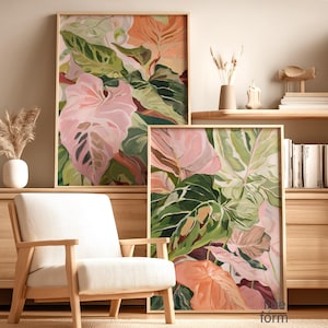 May include: Two framed botanical art prints featuring large, stylized leaves in shades of pink, green, and peach. The artwork is displayed in a light-colored wooden frame. The prints are displayed in a room with a neutral color palette.