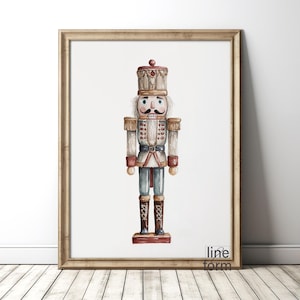 May include: Watercolor print of a nutcracker soldier in a gold frame. The nutcracker is depicted in a traditional uniform with a tall hat, white hair, and a detailed design. The artwork is set against a white background.