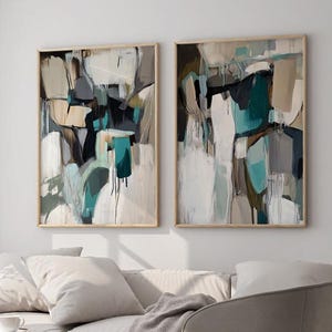 May include: Two abstract paintings in wooden frames. The paintings are in shades of white, gray, black, and teal. The paintings are hung on a white wall.