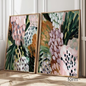 May include: Two framed abstract floral art prints. The artwork features a mix of pink, green, orange, and white brushstrokes. The frames are made of light-colored wood. The overall style is modern and artistic.