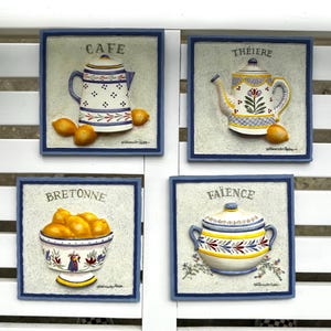 May include: Four framed ceramic wall plaques with a French country theme. Each plaque features a different design: a teapot, a tea kettle, a bowl of lemons, and a lidded pot. The plaques are in a blue frame with the words "CAFE", "THÉIERE", "BRETONNE", and "FAÏENCE".