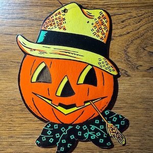 May include: Vintage Halloween decoration featuring a smiling jack-o'-lantern with a yellow hat and a black bow tie with green diamond shapes. The jack-o'-lantern is orange with black eyes and a black mouth. A small broom is in its mouth. Made in the U.S.A.