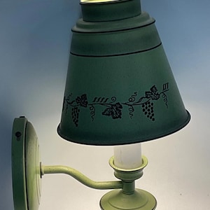May include: A vintage wall-mounted lamp with a green finish. The lamp features a conical shade decorated with a grape vine design. The lamp's arm and base are also green, creating a cohesive look. The lamp is designed to be mounted on a wall.