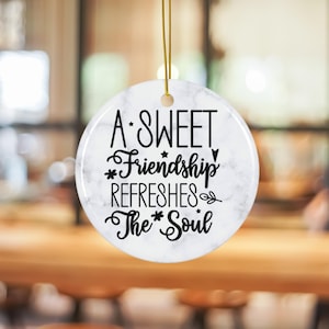 May include: White ceramic ornament with a marble pattern and black text that reads "A Sweet Friendship Refreshes The Soul".