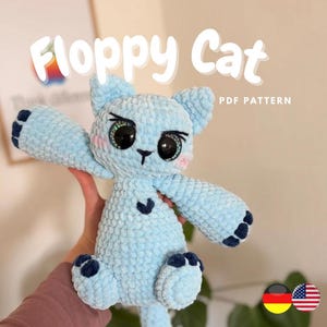 Könnte beinhalten: Ein hellblaues, plüschiges "Floppy Cat"-Spielzeug mit großen, ausdrucksstarken Augen und dunkelblauen Akzenten auf den Pfoten und Ohren. Der Text "Floppy Cat" und "PDF Pattern" ist auf dem Bild zu sehen. Das Spielzeug wird vor einem neutralen Hintergrund gehalten.