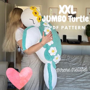 Puede incluir: Una gran tortuga de ganchillo hecha a mano en blanco, verde azulado y amarillo. La tortuga tiene una cabeza blanca con girasoles amarillos, un caparazón verde azulado con flores blancas y amarillas, y el texto "XXL JUMBO Turtle PDF PATTERN". También es visible el identificador de Instagram @irene.thelabel.