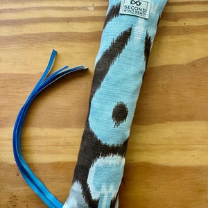 May include: A blue and brown patterned cat toy with a blue ribbon attached. The rectangular toy has a tag that reads "SECOND WIND SEND". The toy is made of fabric and is designed for cats.