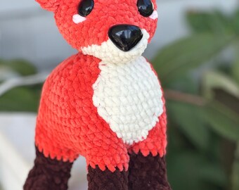 May include: A crocheted fox plush toy with red, white, and brown fur. The fox has black eyes and a black nose.