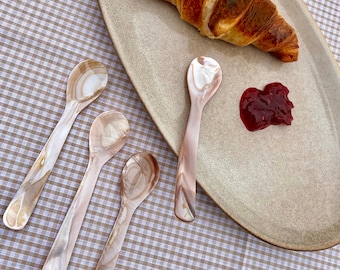 Pode incluir: Quatro colheres de madrepérola em uma toalha de mesa quadriculada com um croissant e geleia em um prato oval bege.