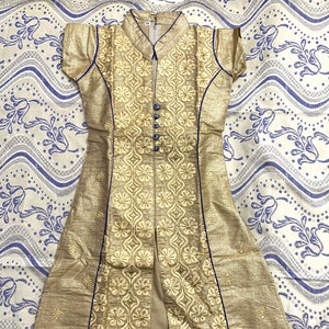 May include: A gold embroidered dress with a blue trim and a button closure. The dress has a short sleeve and a long length.