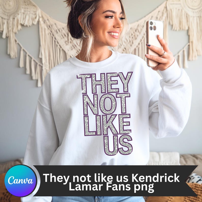 May include: White sweatshirt with the text "THEY NOT LIKE US" in silver glitter letters with purple outlines.
