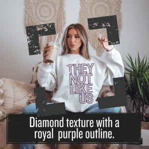 May include: White sweatshirt with the text "THEY NOT LIKE US" in silver glitter with a royal purple outline.