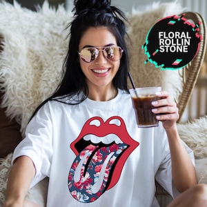 May include: White t-shirt with a red and white graphic of a tongue with a floral pattern. The text "Floral Rollin Stone" is in a circle in the top right corner of the image.