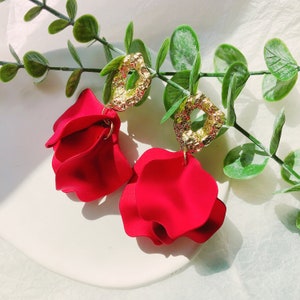 May include: A pair of red flower-shaped dangle earrings with gold textured geometric charms.