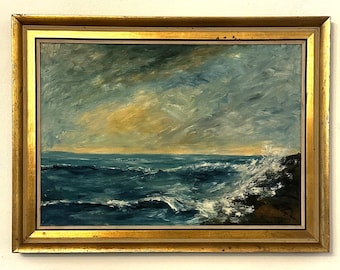 May include: Oil painting of a seascape with a gold frame. The artwork depicts a turbulent ocean with waves crashing against a rocky shore. The sky is a mix of blues, grays, and yellow hues, creating a dramatic atmosphere.