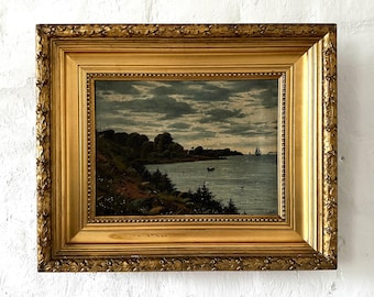 Op de afbeelding: Een ingelijst schilderij dat een zeezicht voorstelt met een bewolkte lucht, een kustlijn met bomen en een paar zeilboten in de verte. Het schilderij is in een gouden lijst.