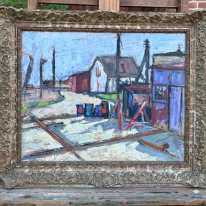 Könnte beinhalten: Ölgemälde einer ländlichen Szene mit Gebäuden, Stromleitungen und Fässern. Das Kunstwerk ist in einem dekorativen, verzierten Goldrahmen gerahmt. Die Farbpalette umfasst Blau-, Rot- und Weißtöne mit einem strukturierten, impressionistischen Stil.
