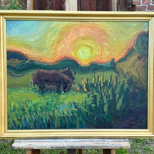 May include: Oil painting in a gold frame depicting a sunset over a field with two dark brown animals. The sky transitions from blue to yellow and orange. Green grass and tall plants fill the foreground.