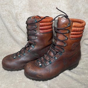 May include: A pair of brown leather hiking boots with black laces and metal eyelets. The boots have a padded, reddish-brown collar and show signs of wear. The soles are dark, and the boots appear sturdy.