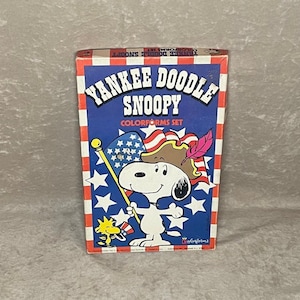 May include: A vintage box of Yankee Doodle Snoopy Colorforms featuring a cartoon image of Snoopy dressed as a colonial soldier holding an American flag. The box is red, white, and blue with stars and stripes.