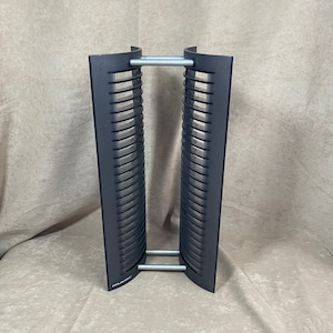 May include: A black CD storage tower with a silver metal frame. The tower has two sections, each with 24 slots for CDs. The tower is labeled "Atlantic" at the bottom.