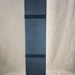 May include: A tall, black, rectangular display stand with a square base. The stand has a textured surface and is divided into three sections with dark bands. The base has a red accent.