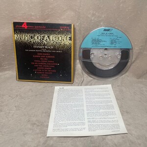 May include: A black and gold box with the title "Music of a People" by Stanley Black. The box contains a reel-to-reel audio tape with a black and silver label. The label lists the songs on the tape, including "Hava Nagila", "Raisins and Almonds", and "Tzena Tzena Tzena".