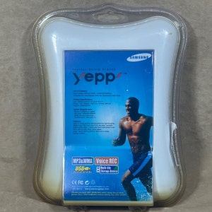 May include: A white plastic package with a blue background showing a man swimming. The package is for a Samsung Yepp digital audio player. The player features MP3 and WMA playback, voice recording, and a USB connection. The text "MP3&WMA" and "Voice REC" are printed on the package.