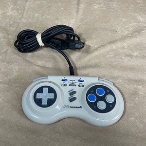 May include: A white PC Propad 4 controller with a black cord and a gray and blue button layout. The controller has a directional pad, four buttons, and a speed selector.