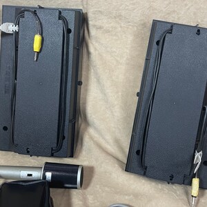 May include: Two black speaker bases with wires and yellow connectors. A silver microphone with a black microphone cover and a black stand is in the foreground.