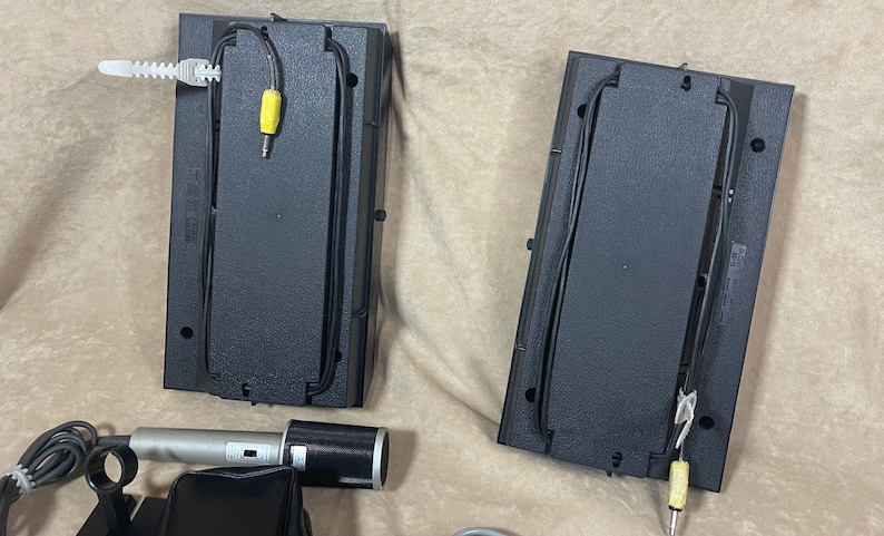 May include: Two black speaker bases with wires and yellow connectors. A silver microphone with a black microphone cover and a black stand is in the foreground.