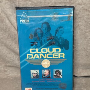 May include: A blue VHS tape case with a picture of three people on the front. The title of the movie is "Cloud Dancer" and the actors are David Carradine, Jennifer O'Neill, and Joseph Bottoms. The case is labeled "Prism Entertainment" and "VHS".
