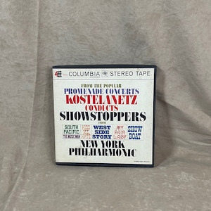 May include: A black and white Columbia Records stereo tape cassette featuring a red and white image of conductor Andre Kostelanetz conducting the New York Philharmonic Orchestra. The tape features music from the popular Promenade Concerts, including "South Pacific", "Kiss Me, Kate", "West Side Story", "My Fair Lady", and "Show Boat".