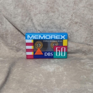 May include: A blue and red cassette tape case with the brand name "Memorex" and the text "Type I Normal Bias" printed on the front. The case also has a green and yellow label with the text "DBS 60" printed on it.